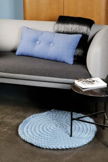 Lichtblauw vloerkleed met lichtslang in een woonkamer. Verder staat een grijze bank met een blauw kussen en een zwart dekentje afgebeeld, net als een bruin bijzettafeltje.