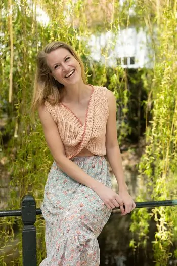 Model draagt de roze, zomerse wikkeltop boven een fleurige rok.