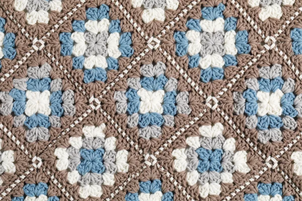 Close-up gehaakte schort van granny squares, het motief is hierop goed te zien. Het bevat de kleuren taupe, ivoor, lichtblauw en grijs.